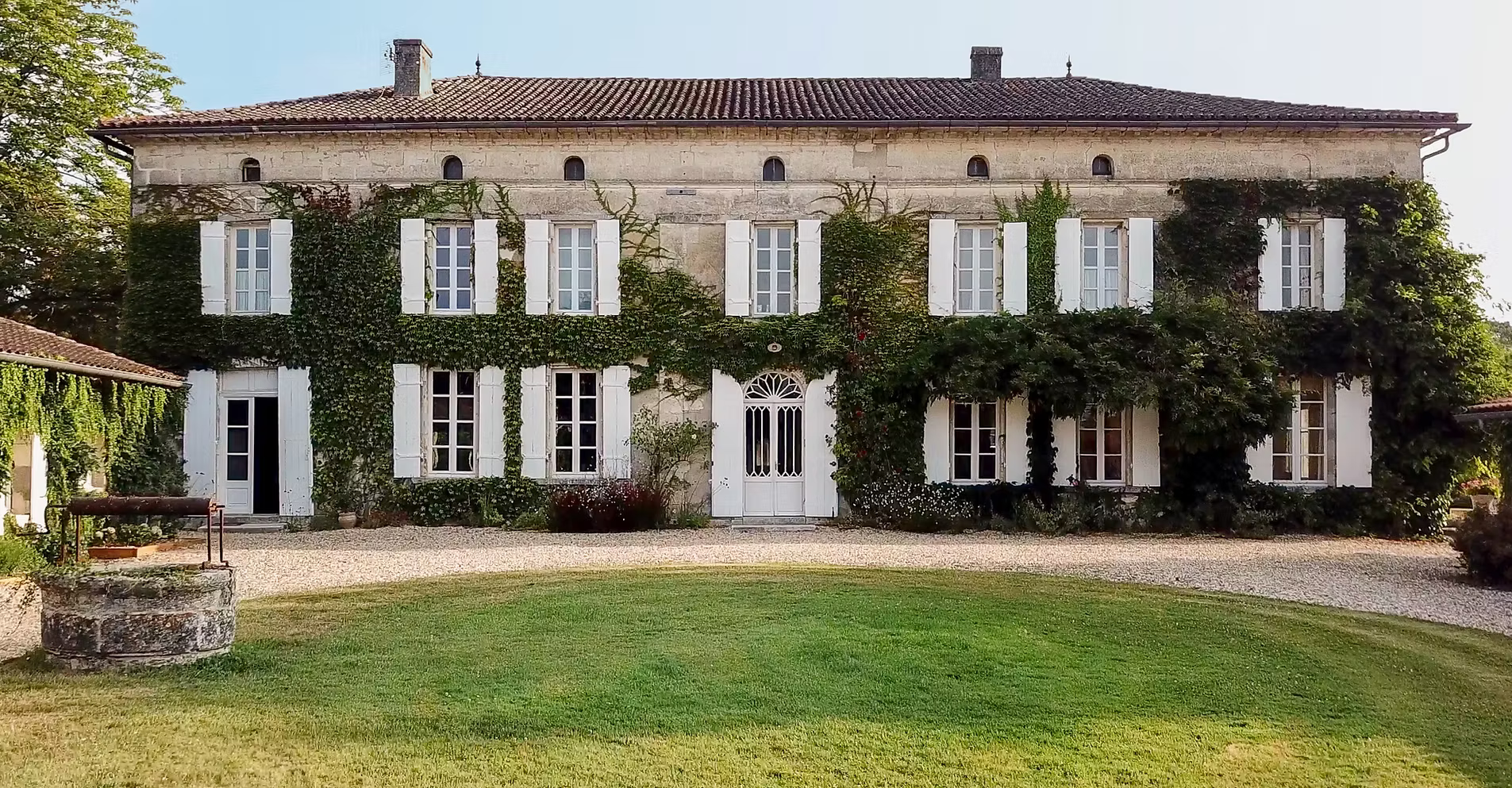Beautiful ivy-clad chateau with white shutters, green lawn, and stone well.