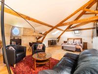 Vue intérieure de la Suite l’Estuaire avec lit queen-size, coin salon, poutres apparentes et décoration raffinée au…