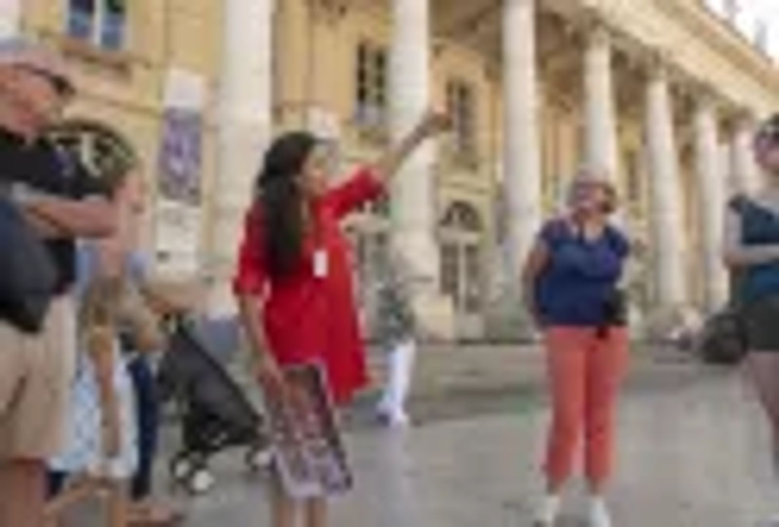 Une guide touristique en robe rouge fait une visite guidée devant le Grand Théâtre de Bordeaux, en montrant…