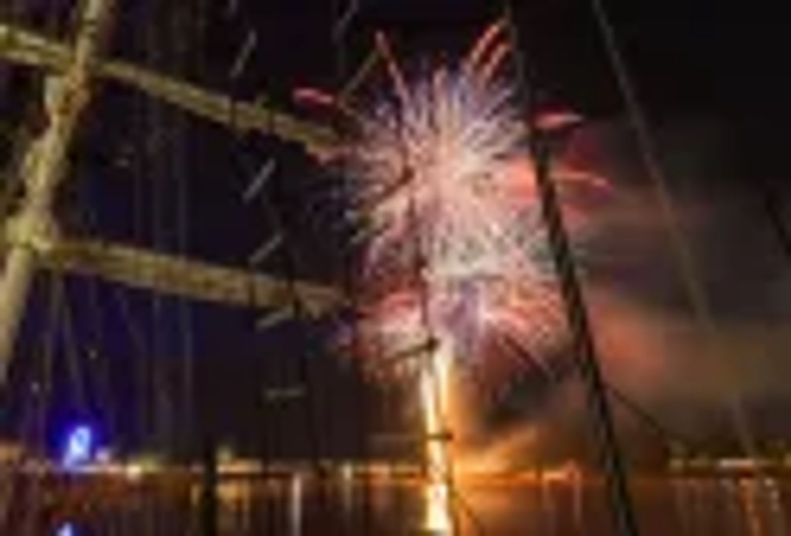Feu d'artifice multicolore illuminant le ciel nocturne de Bordeaux, vue depuis un voilier avec la Grande Roue et les…
