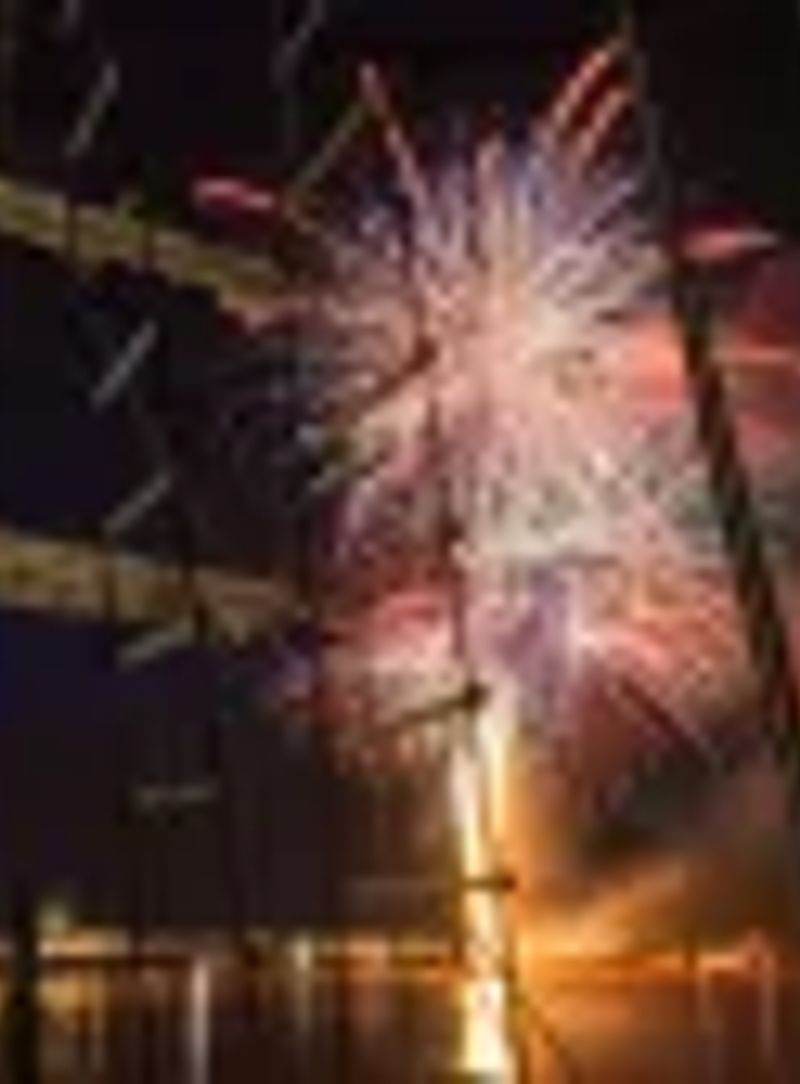 Feu d'artifice multicolore illuminant le ciel nocturne de Bordeaux, vue depuis un voilier avec la Grande Roue et les…