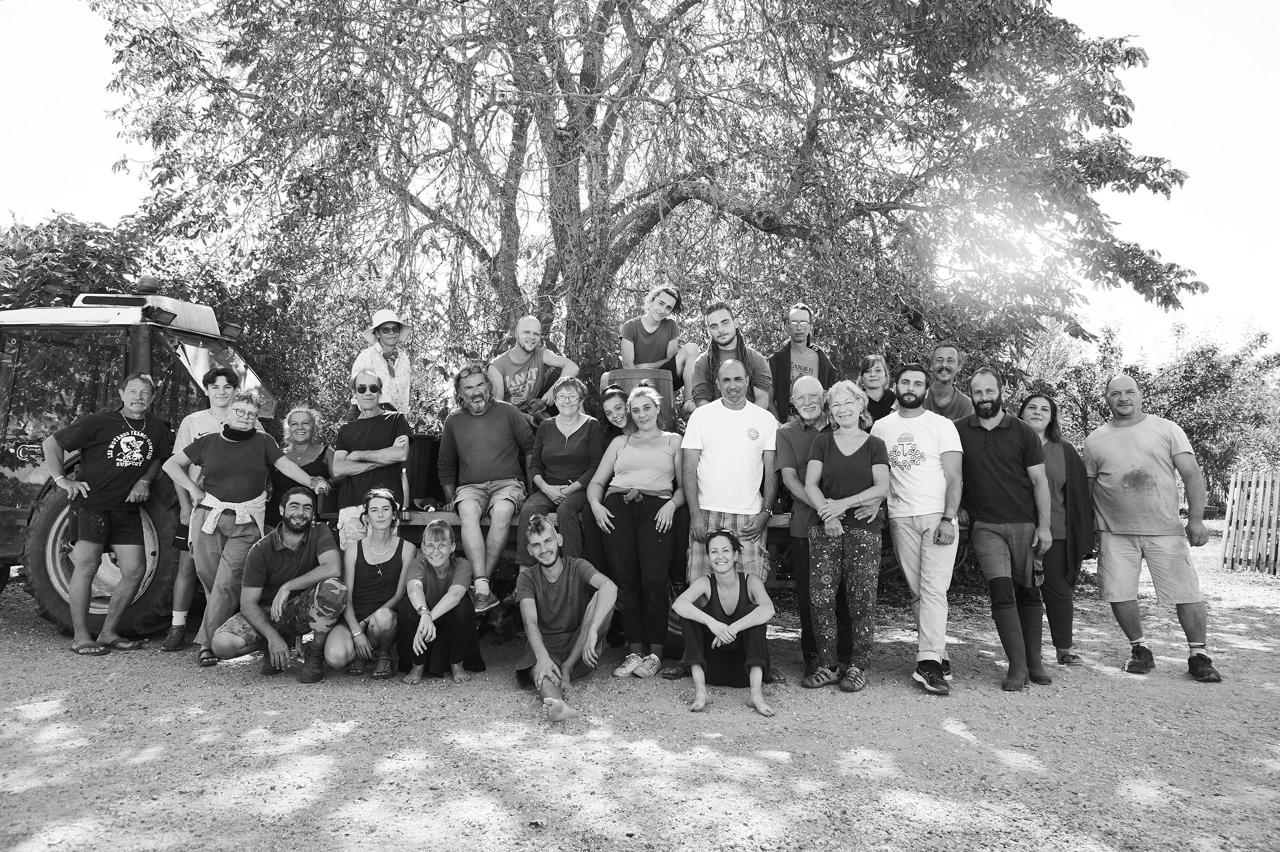 Groupe de 28 personnes posant devant un arbre et un tracteur en plein air par une journée ensoleillée.