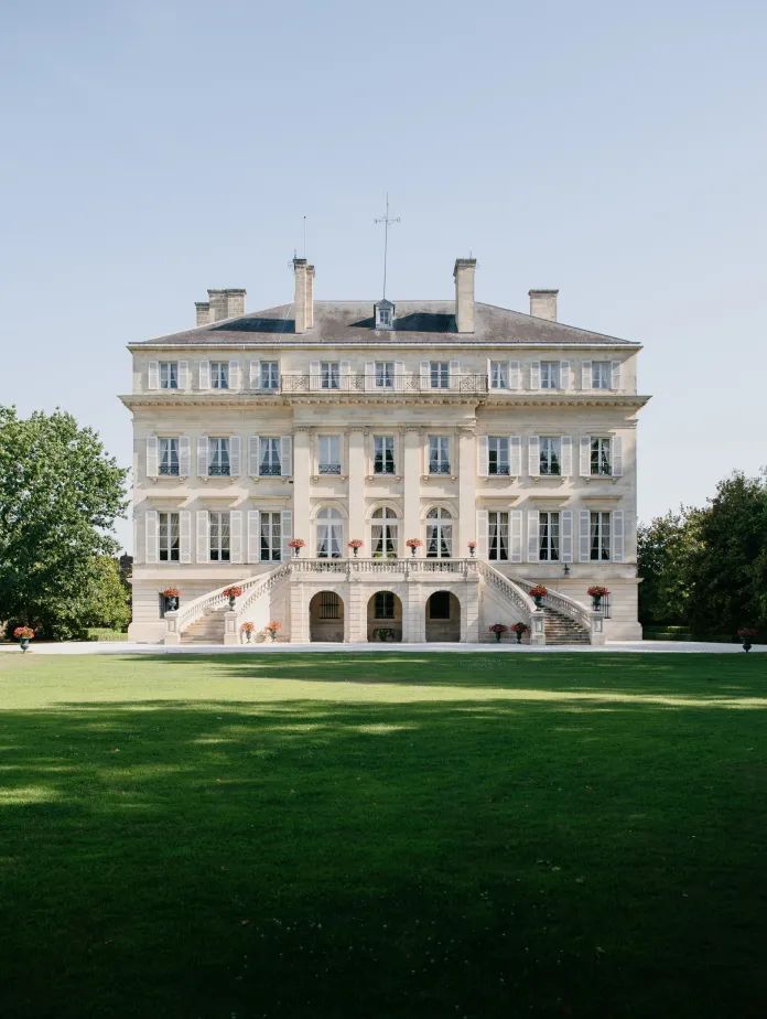 A grand, multi-storied building with a symmetrical façade, set on lush green grounds under a clear blue sky.